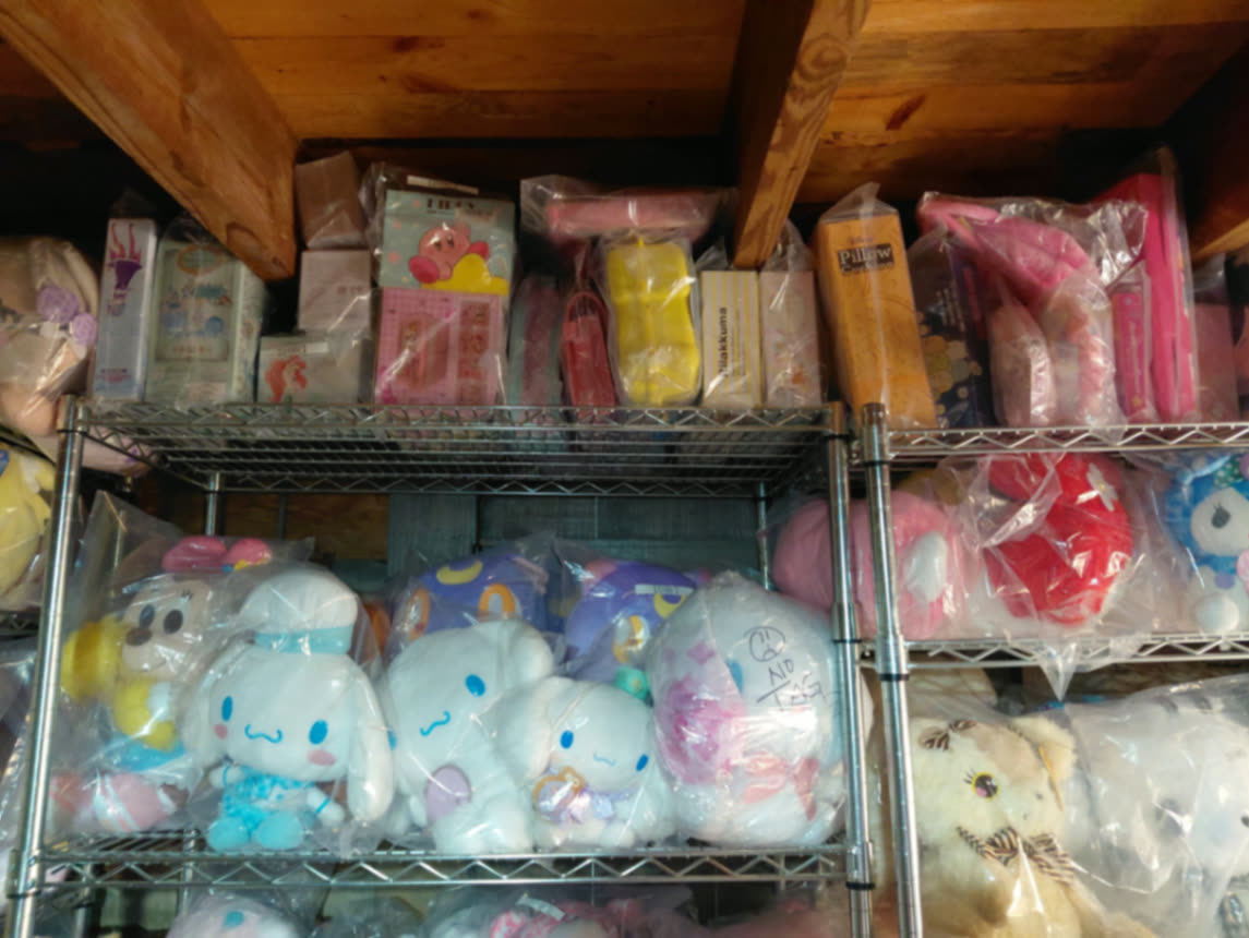 Shelf of sealed Cinnamoroll plush under the cabin's wooden ceiling beams with boxed goods above