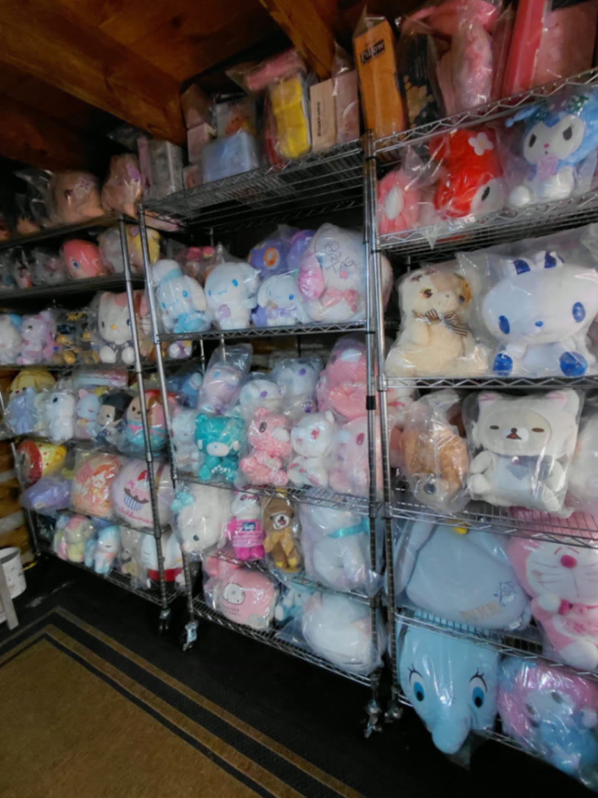 Shelving aisle under the cabin's wooden beams filled with sealed Cinnamoroll, Rilakkuma, and Doraemon plush