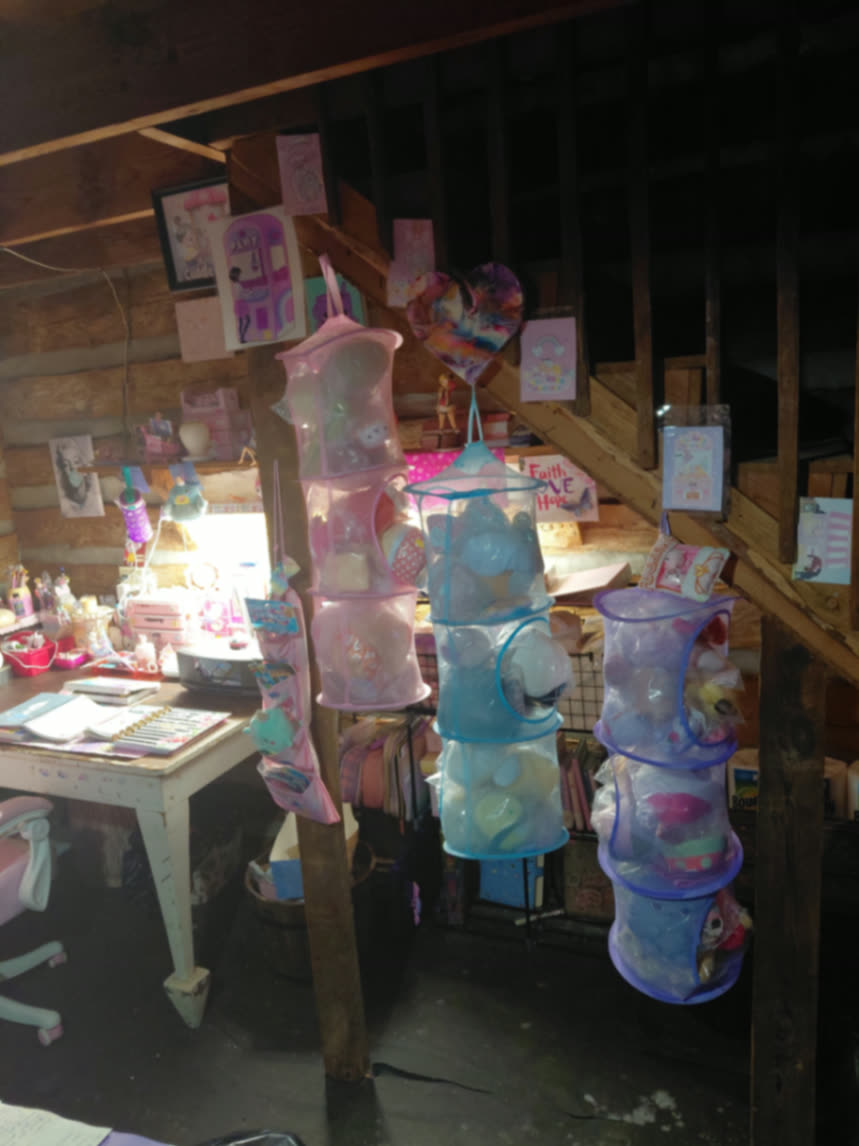 Hanging mesh plush organizers by the cottage staircase with kawaii art taped to the log walls