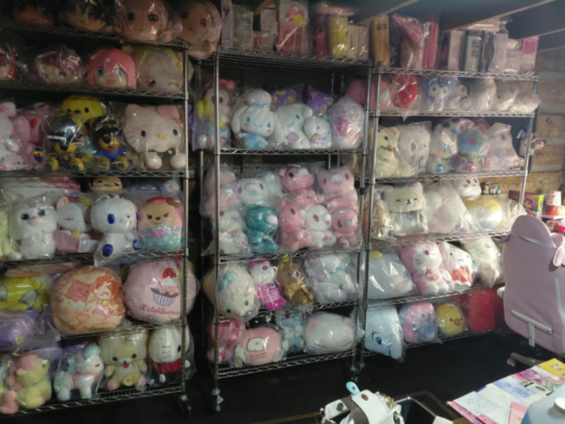 Wide view of the cottage prize room with three chrome shelving units packed with sealed Japanese plush