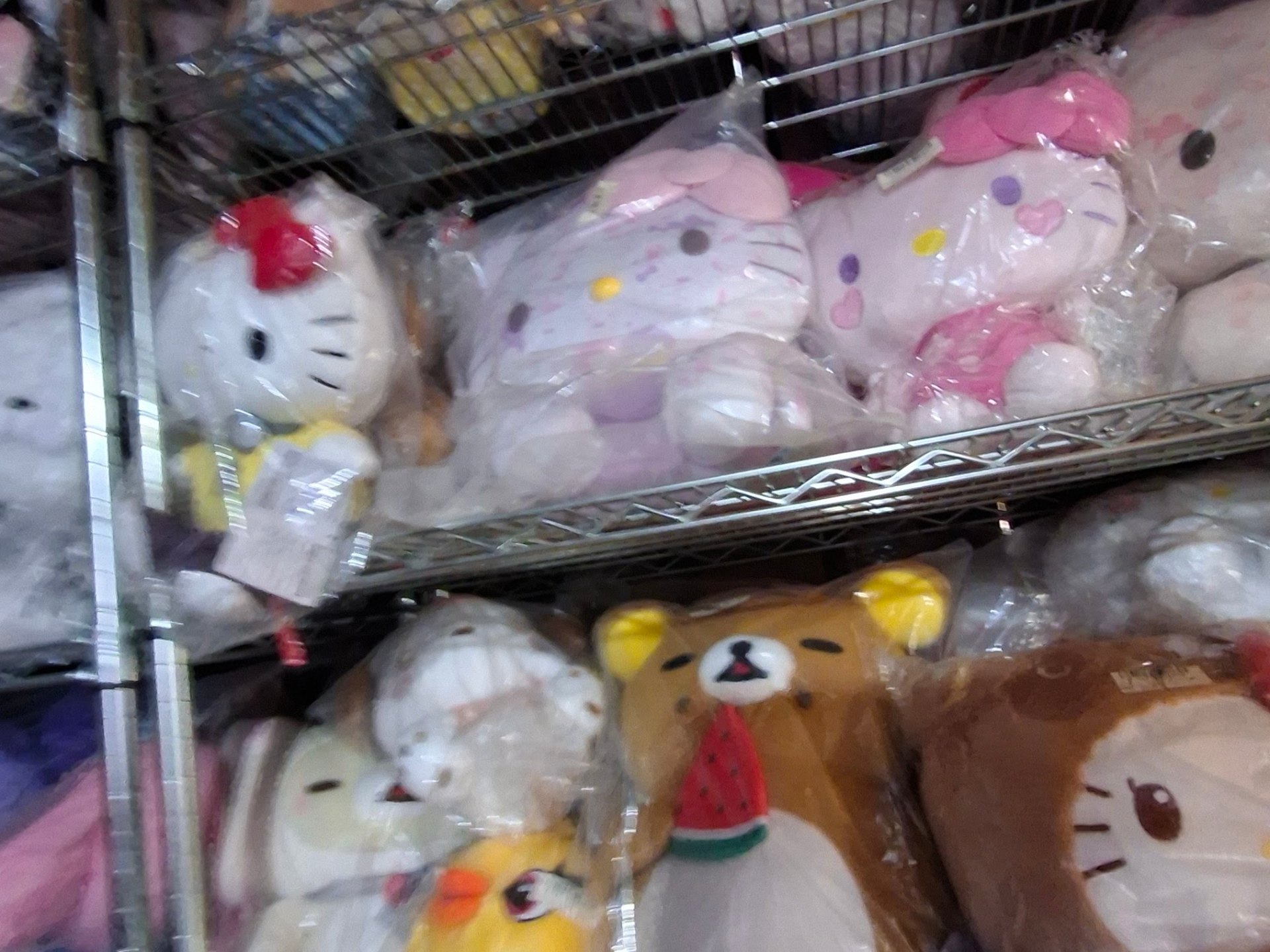 Close-up of sealed Hello Kitty and Rilakkuma plush prizes tucked side by side on a wire shelf